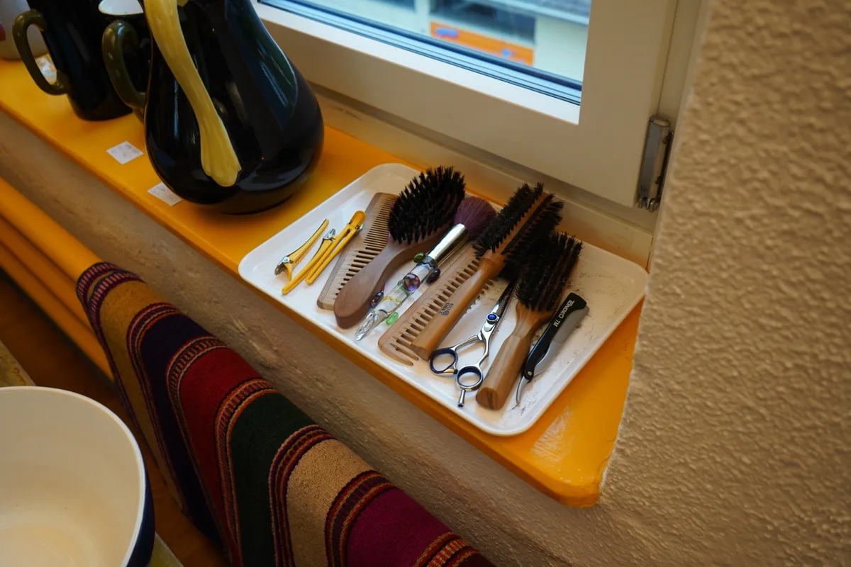 Auf einem Tablett am Fenster: diverse Haarbürsten, Haarspangen, Pinsel und eine Schere.